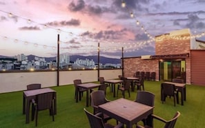 An outdoor seating area with tables and chairs, a grassy lawn, and a cityscape view in the background. - NO.25 HOTEL Namchuncheon (Chuncheon)