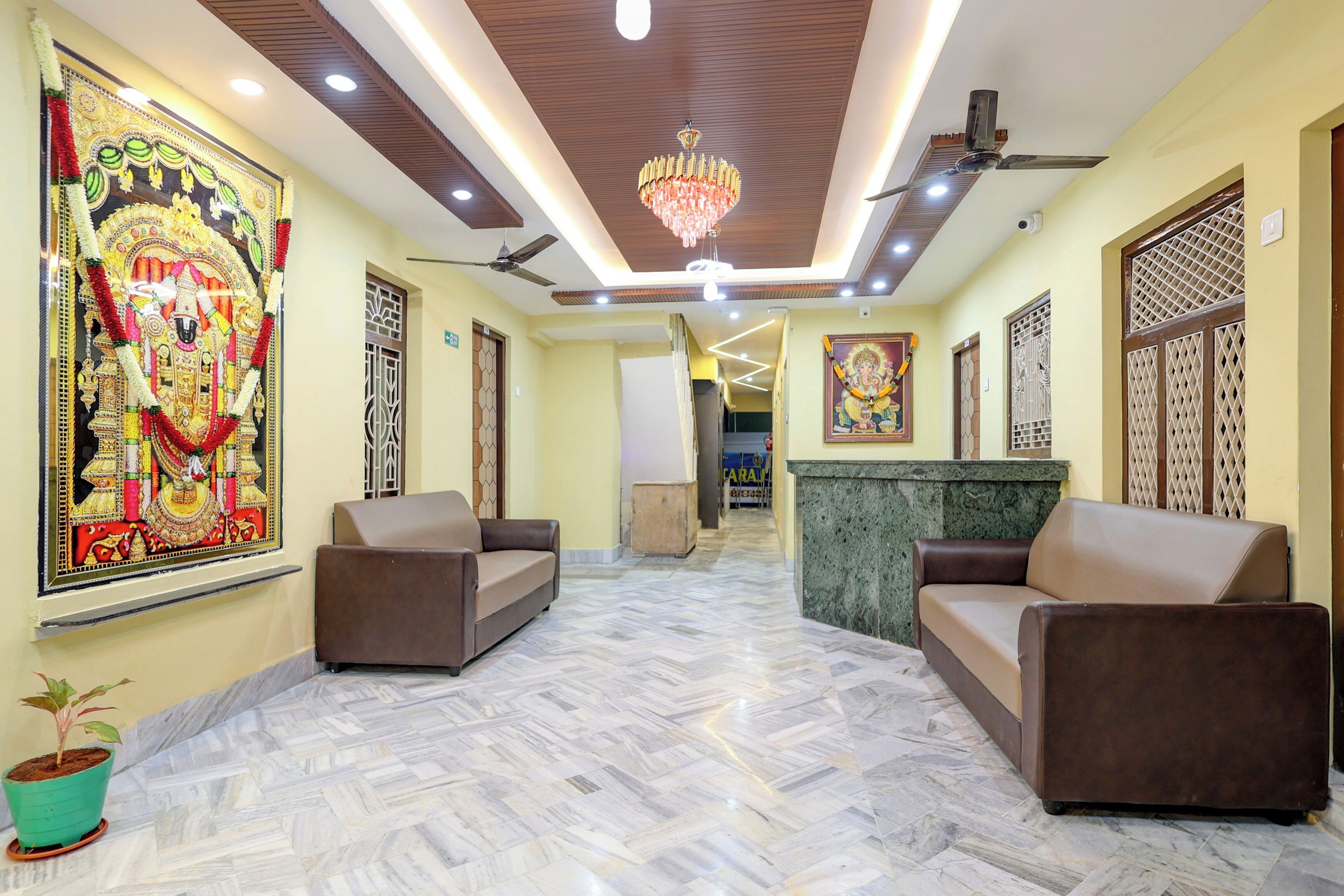 A spacious lobby with a marble floor, two sofas, a chandelier, ceiling fans, and a large religious painting.