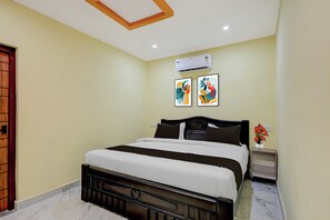 A hotel room with a bed, a nightstand, a vase with flowers, and two wall art pieces.
