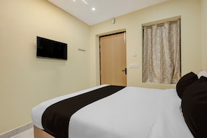 A hotel room with a bed, a television mounted on the wall, a door, and a window with a curtain. - Super Hotel O Seven Road Junction (Srikakulam)