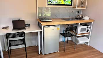 Eine kompakte Küchenzeile mit integriertem Mikrowellenherd, einem kleinen Kühlschrank und einem Spülbecken. Auf einem weißen Schreibtisch steht ein Laptop, und es gibt zwei schwarze Stühle.