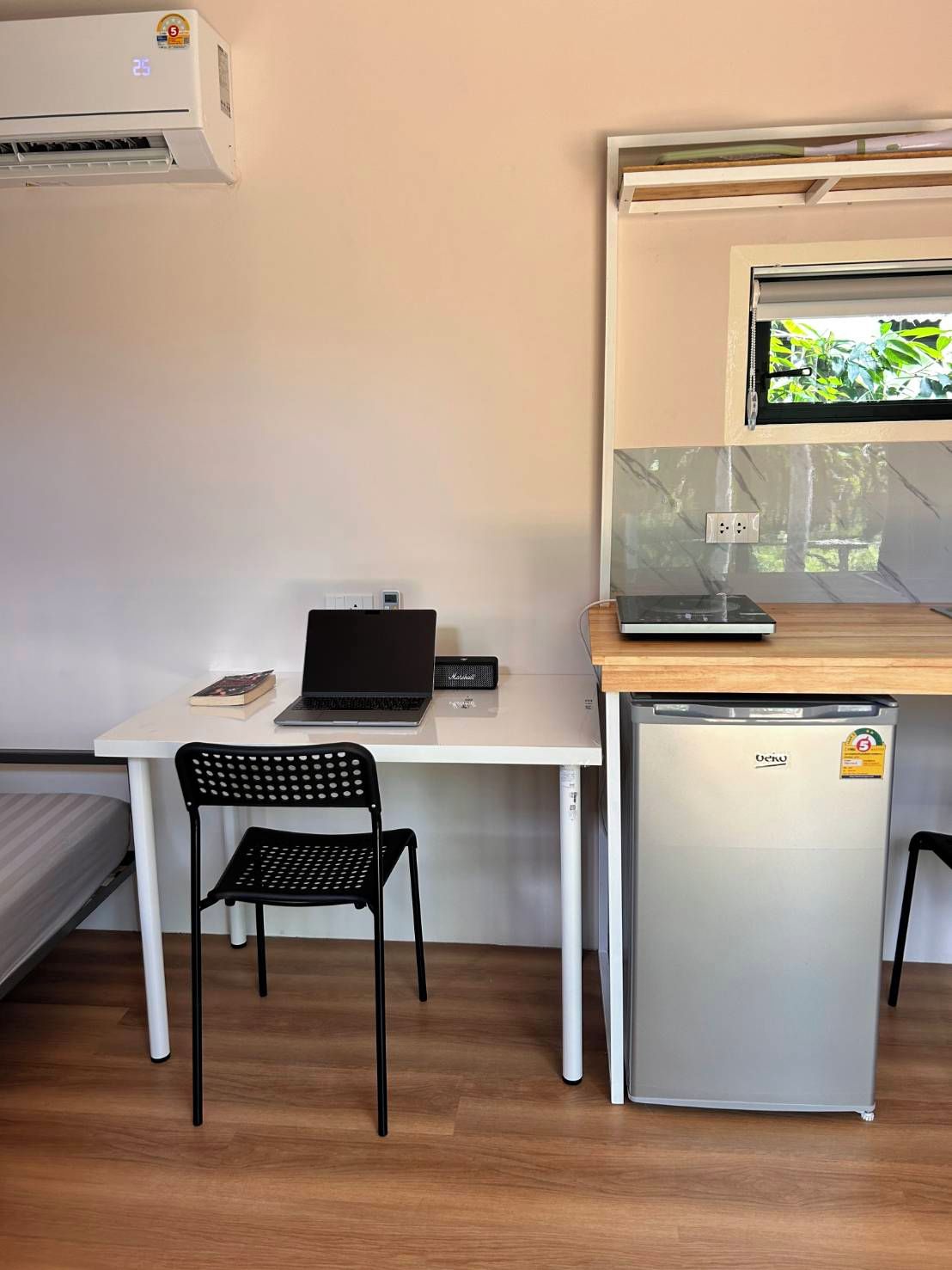 A compact kitchenette with a refrigerator, a small sink, and a window with a view of greenery.