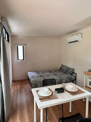 Quarto compacto com cama, uma pequena mesa posta para dois e uma janela.