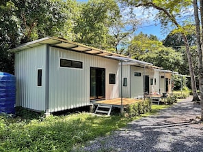 A row of single-story mobile homes with external wooden decks, surrounded by greenery and trees. - Melinjo Garden Big Buddha  (Chalong)