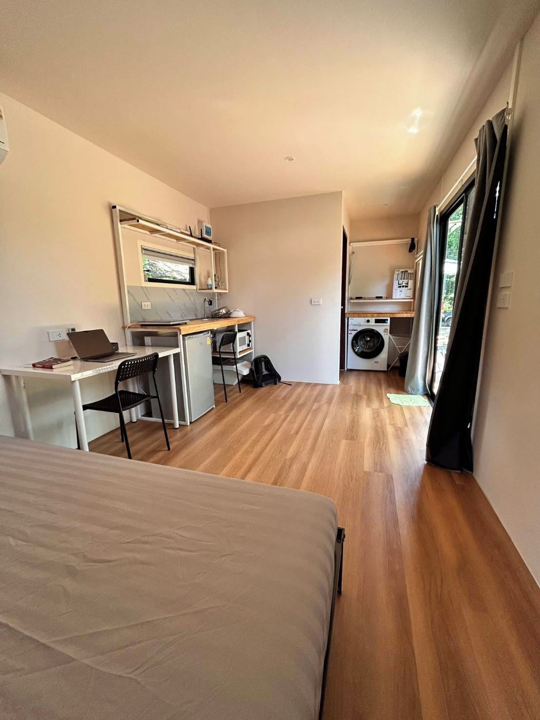 A compact hotel room with a bed, a desk with a laptop, a microwave, and a washing machine.