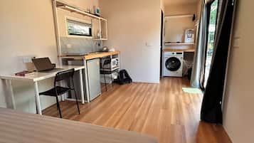 A compact hotel room with a bed, a desk with a laptop, a microwave, and a washing machine.