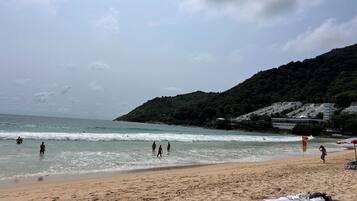 Une plage où l’on voit des gens nager et se promener, un rivage sablonneux et, au loin, une colline parsemée de bâtiments.