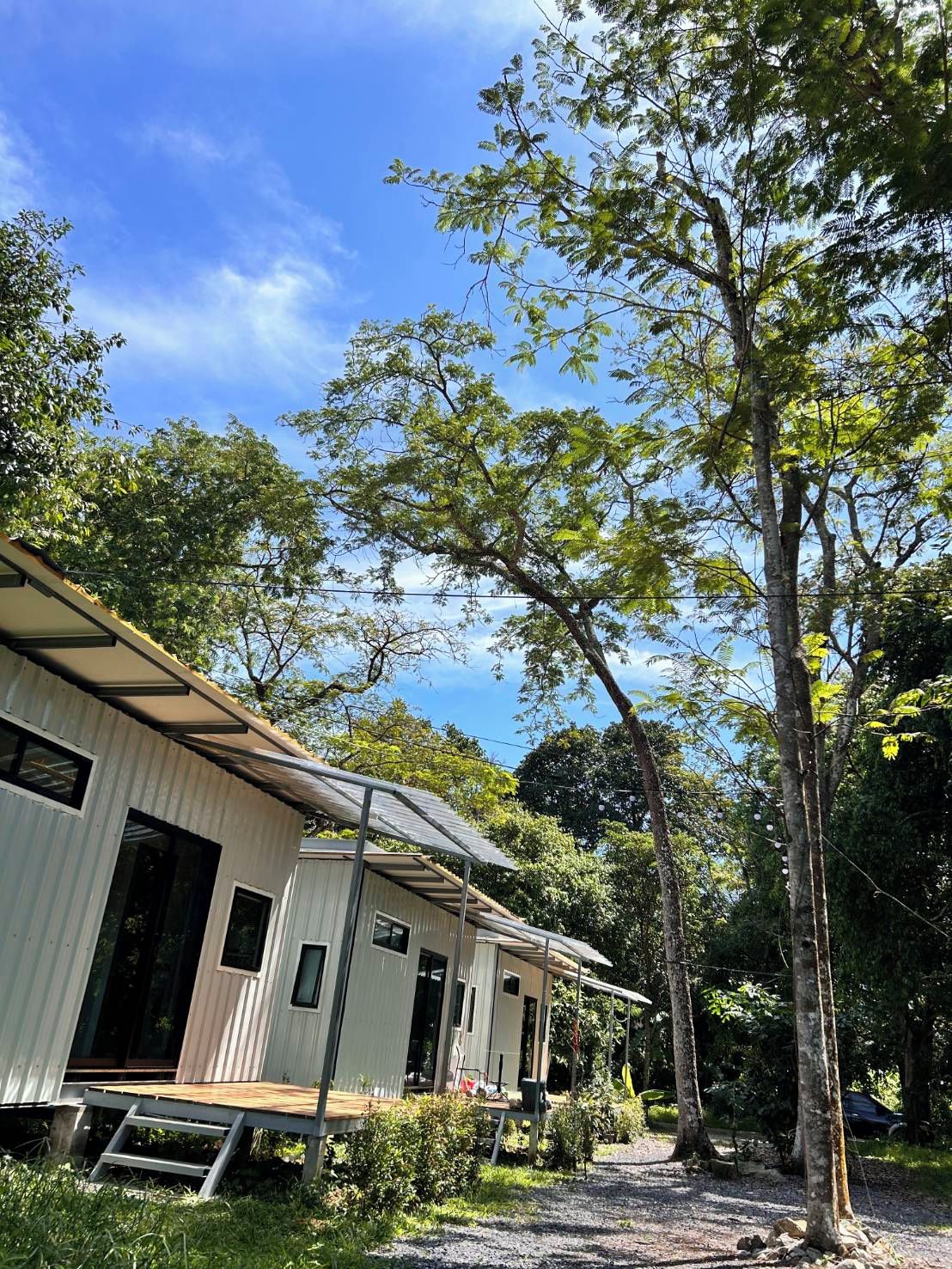 A row of single-story cabins with a covered porch area, surrounded by trees and a clear sky.