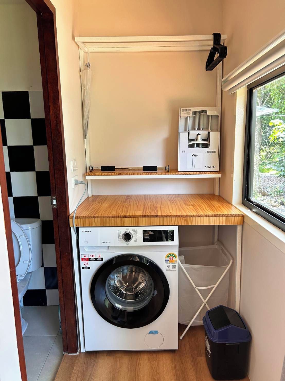 Une petite buanderie équipée d’un lave-linge, d’un sèche-linge et d’une petite poubelle.