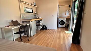 Ein kleines Zimmer mit einem Bett, einem Schreibtisch, einem Stuhl, einer Mikrowelle, einer Waschmaschine und einem Fenster.