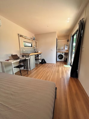 Ein kleines Zimmer mit einem Bett, einem Schreibtisch, einem Stuhl, einer Mikrowelle, einer Waschmaschine und einem Fenster.