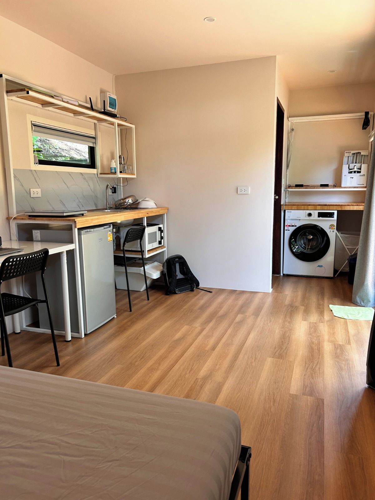 A compact room with a kitchenette, a washing machine, a bed, and a chair.