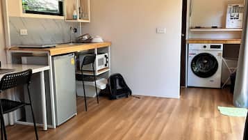 A compact room with a kitchenette, a washing machine, a bed, and a chair.