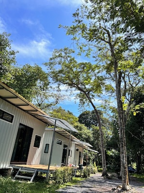 A row of single-story buildings with a metal roof, surrounded by trees and greenery. - Melinjo Garden Big Buddha  (Chalong)