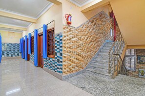 A hallway with a staircase leading to a landing, a fire extinguisher mounted on the wall, and a patterned wall.