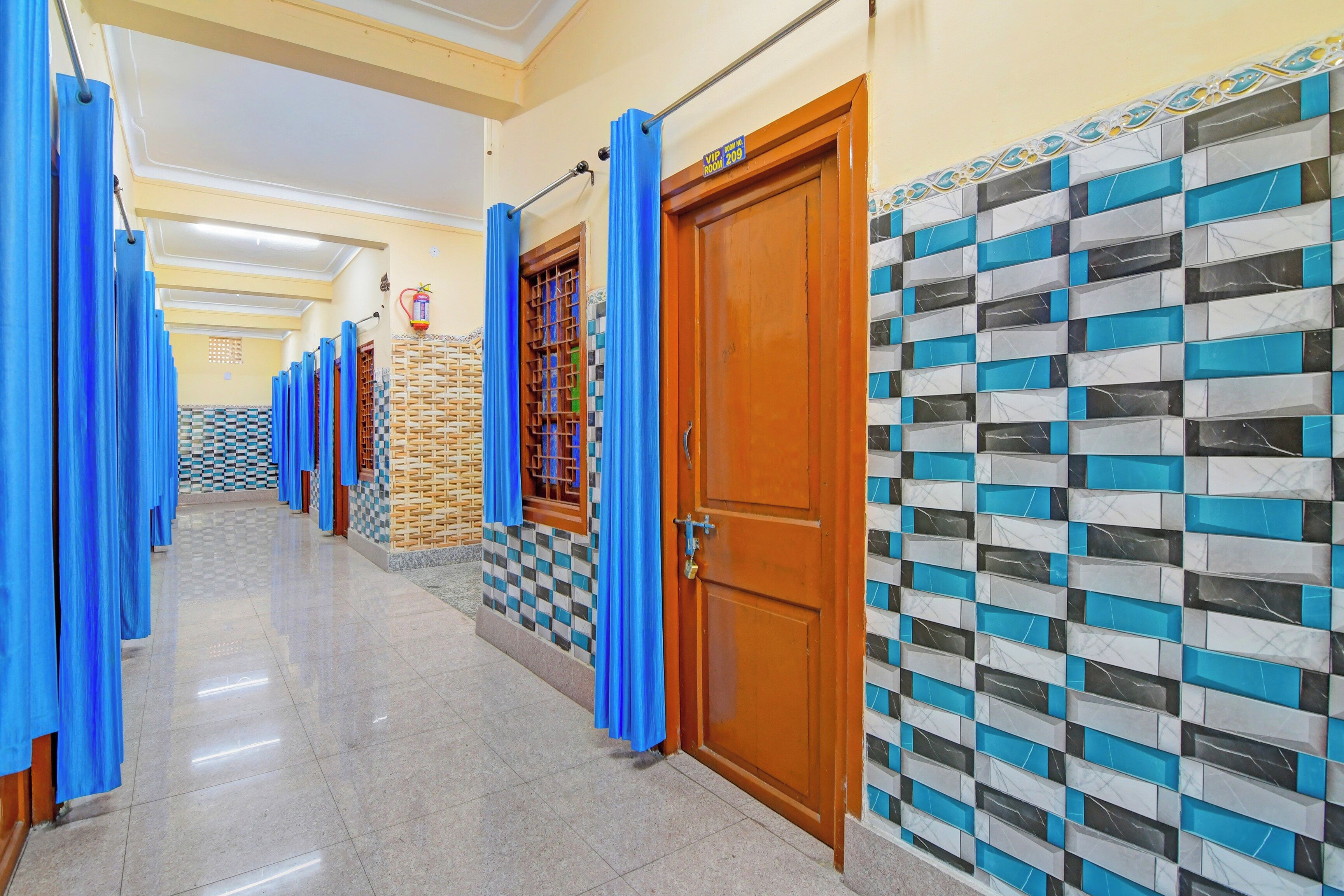 A hotel corridor with blue curtains, a fire extinguisher, a checkered wall, and a wooden door.