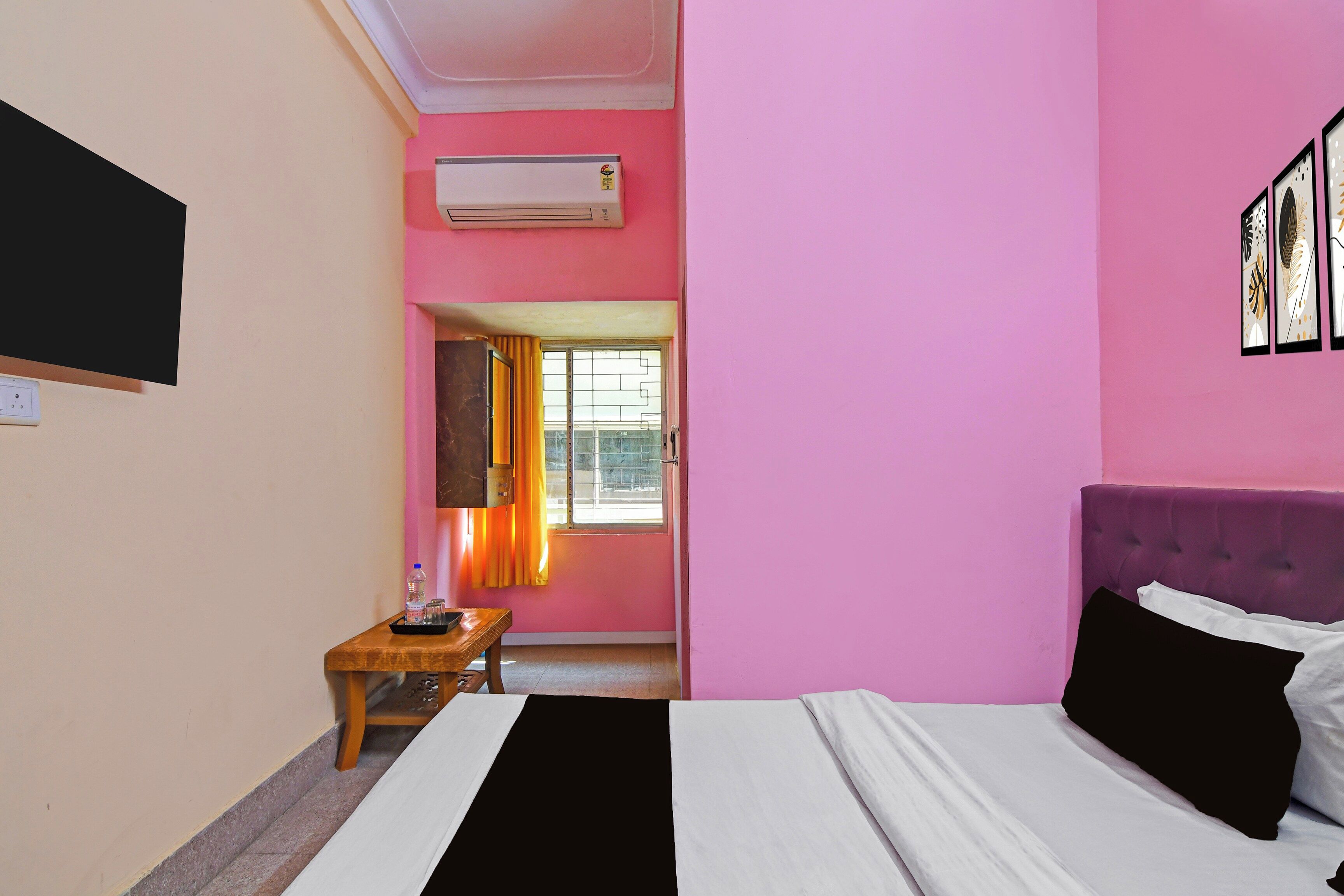 A room with a bed, a small table, a water bottle, a mirror, and a window with curtains.