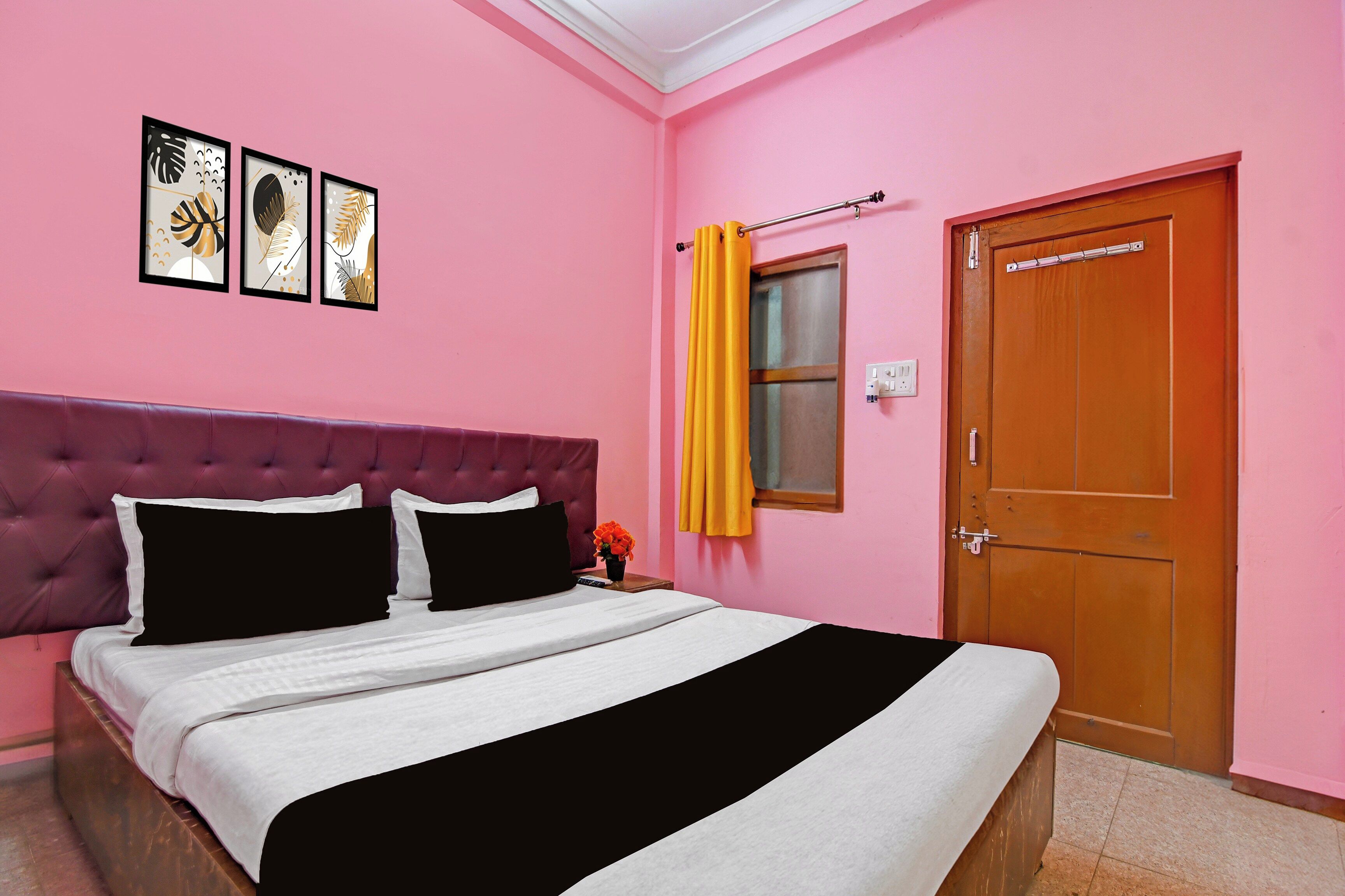A bedroom with a pink wall, a tufted headboard, a bed with white and black bedding, and a wooden door.