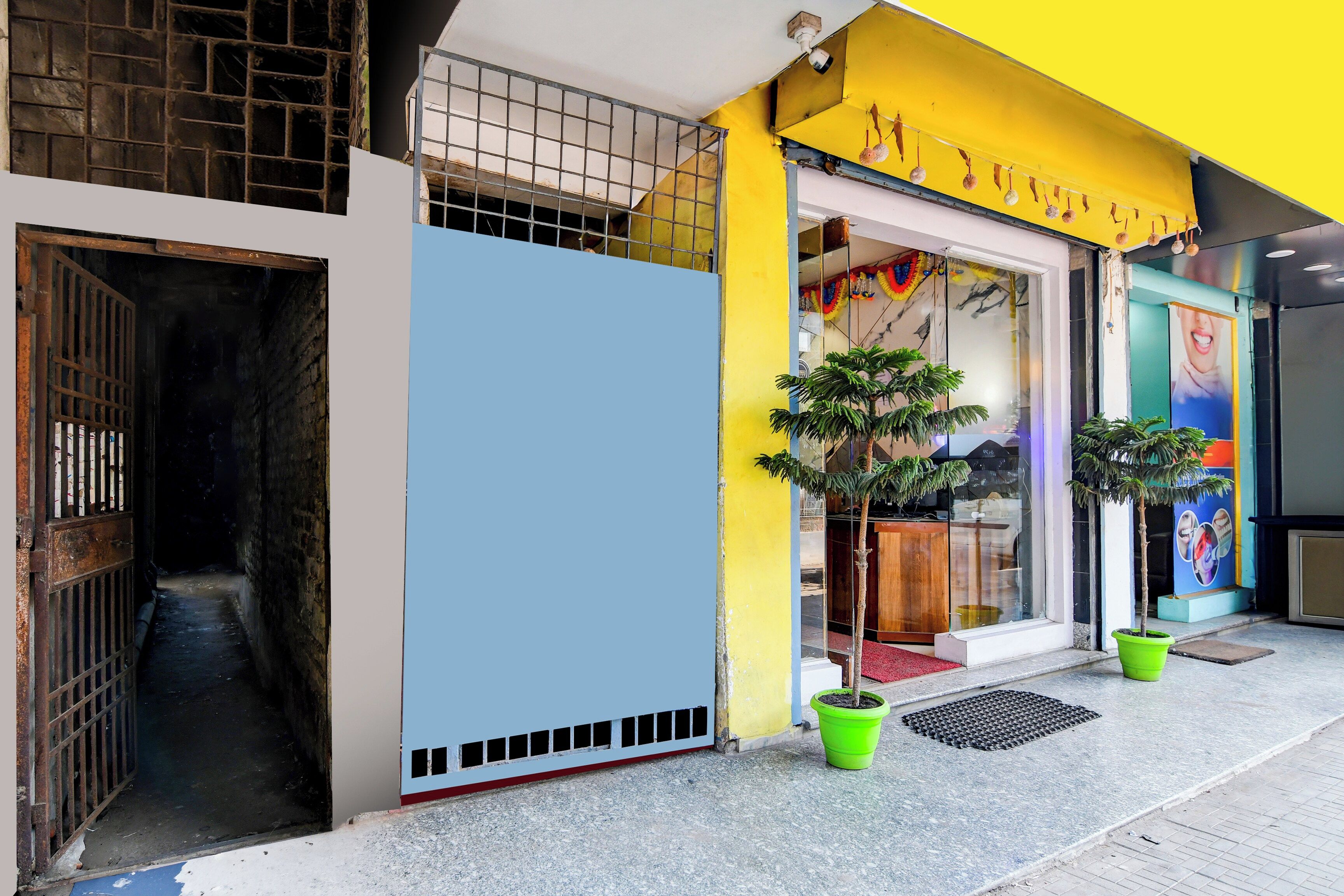 Una entrada de edificio con una reja metálica, un muro azul y un toldo amarillo.
