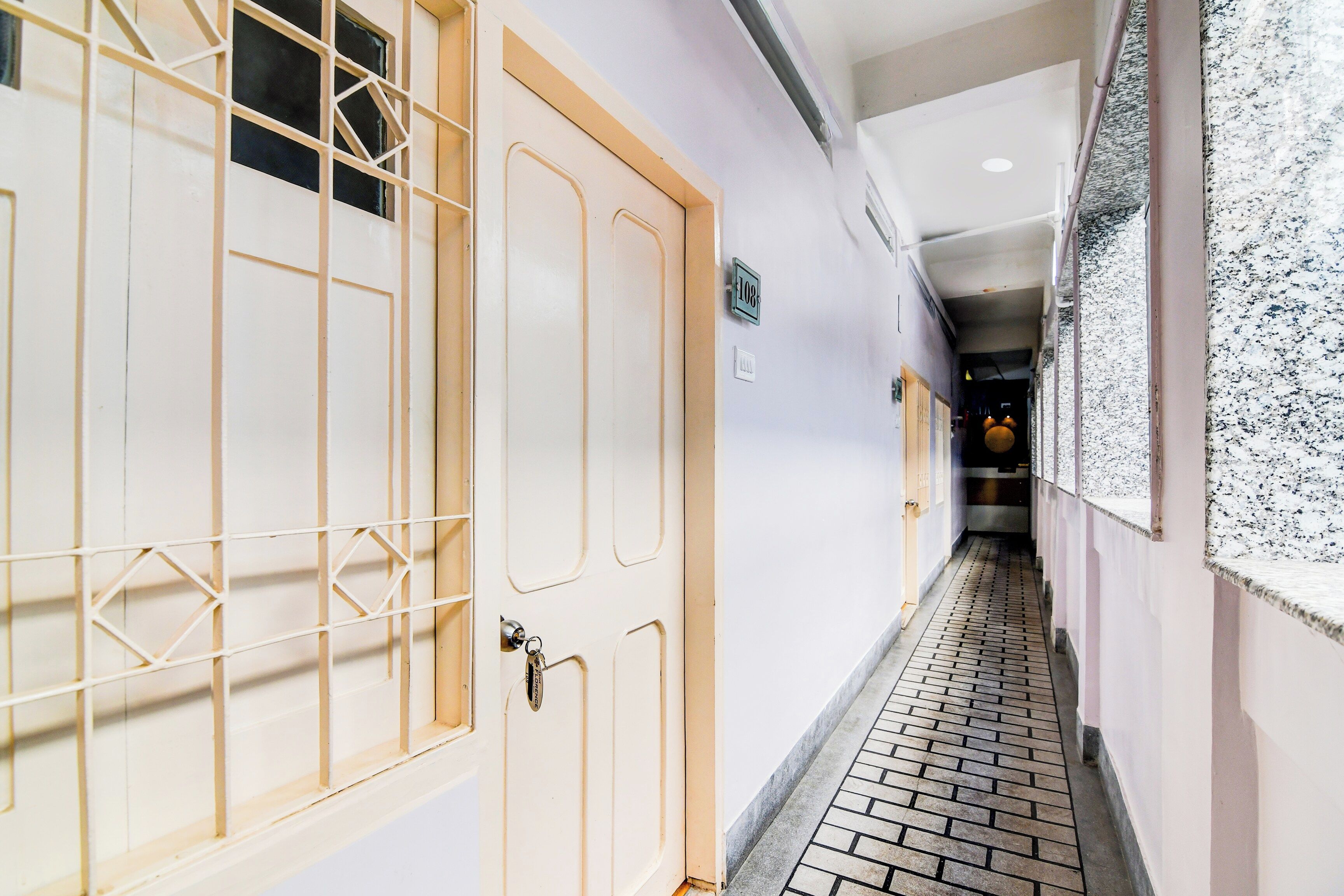 A narrow hallway with a tiled floor, a door with a keyhole, and a wall-mounted number sign.