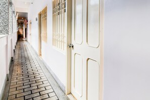 Un pasillo estrecho con suelo de baldosas, paredes blancas y una puerta con reja de metal.