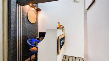 Zona de recepción con un mostrador, una silla azul, un letrero en la pared y un adorno en la parte superior.