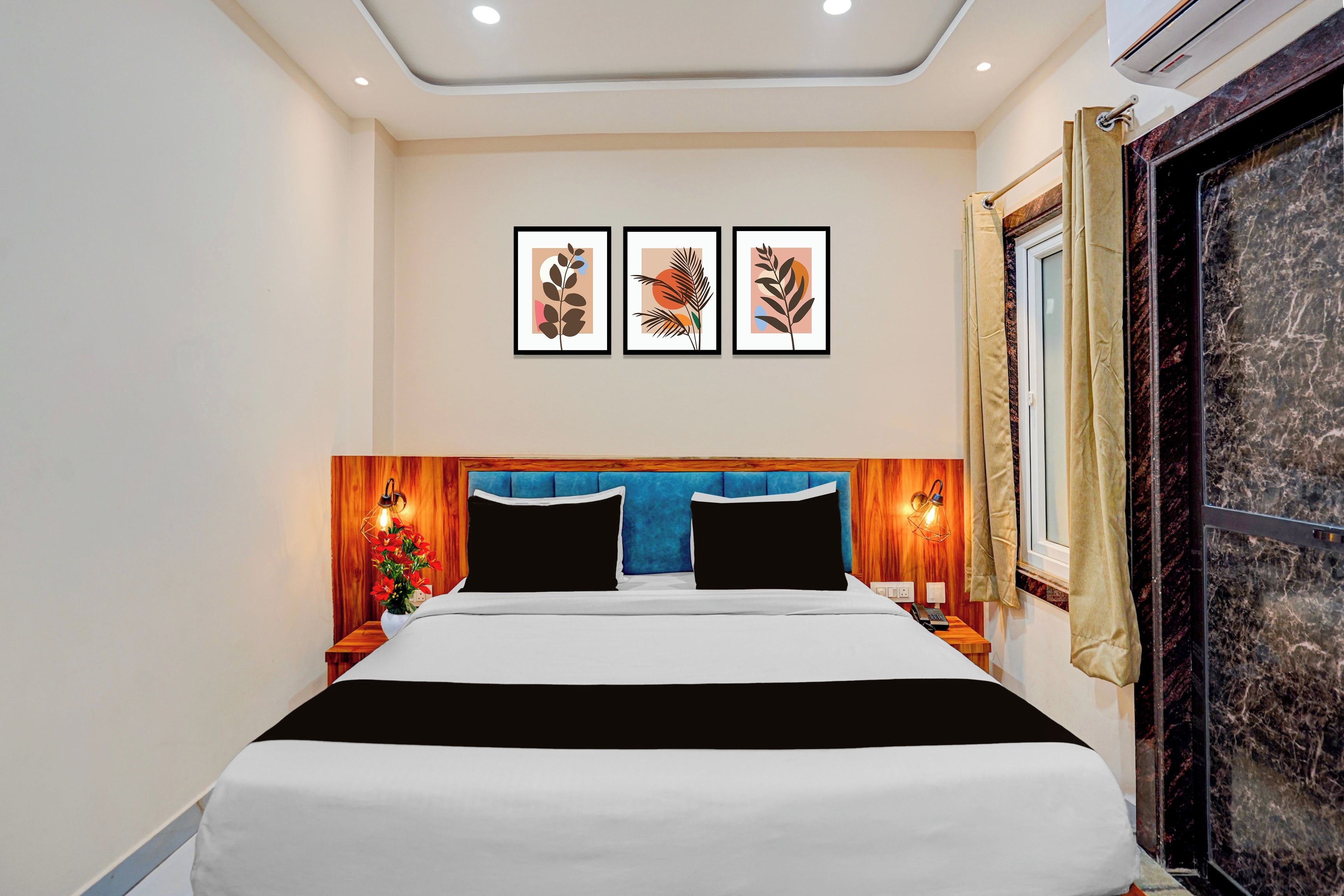 Quarto de hotel com cama, cabeceira de madeira, luminárias fixadas na parede e quadros acima da cama.