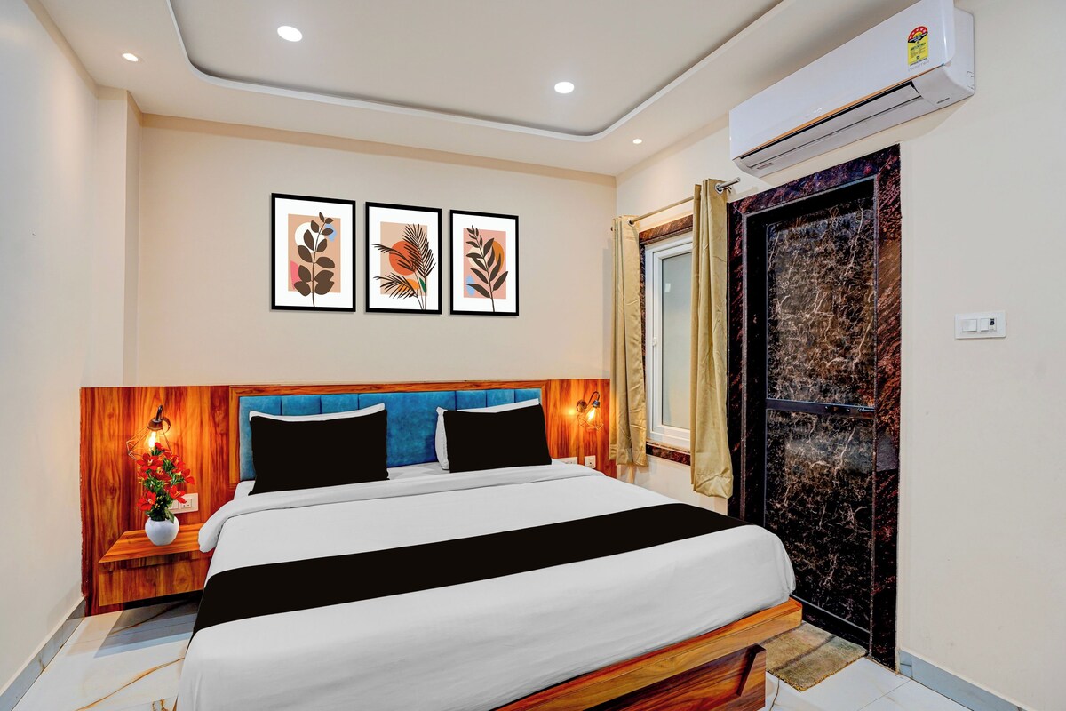 Habitación de hotel con cama, mesita de noche, aire acondicionado de pared y cuadros enmarcados sobre la cama.