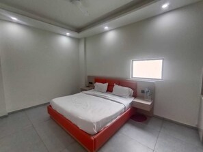 Un dormitorio con cama, mesita de noche, ventana y lámpara de techo.
