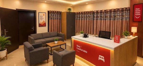 Zona de recepción de un hotel con un sofá, sillas, mostrador de recepción y un cartel que dice 'Stay Comfortable'.