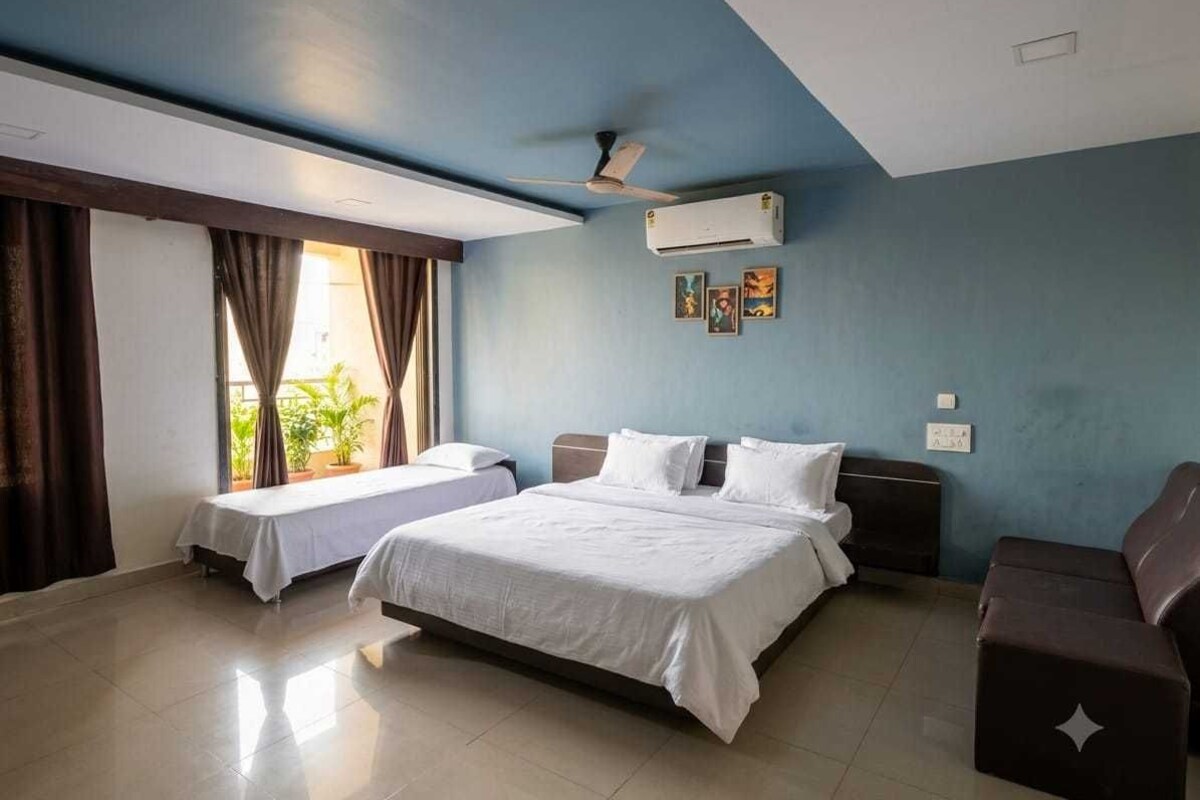 A hotel room with a large bed, a smaller bed, a sofa, a ceiling fan, and an air conditioning unit.