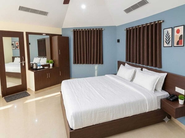A hotel room with a large bed, a wardrobe, a bedside table with a phone, and a small plant.