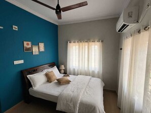 A bedroom with a bed, a ceiling fan, a window with curtains, and wall-mounted air conditioning.