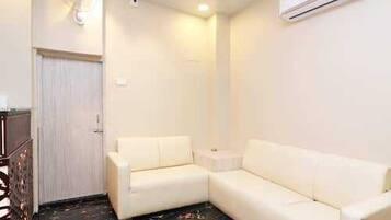 A room with a white sofa, a small side table, a ceiling fan, and an air conditioning unit.
