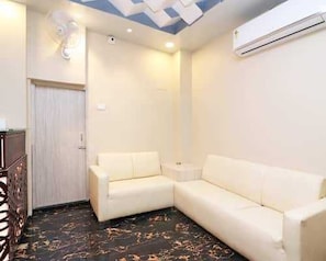 Una habitación con un sofá blanco, una mesita auxiliar, un ventilador de techo y un equipo de aire acondicionado.
