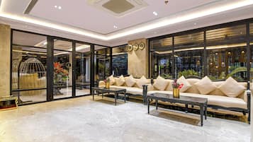A spacious lobby with a marble floor, a sofa set, a coffee table, and a large window with decorative elements.