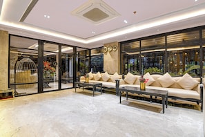 Un vestíbulo amplio con piso de mármol, un conjunto de sofás, una mesa de centro y un ventanal con detalles decorativos.