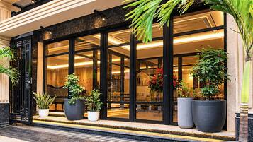 Entrada de hotel con amplias puertas de cristal, plantas en macetas e interior bien iluminado.