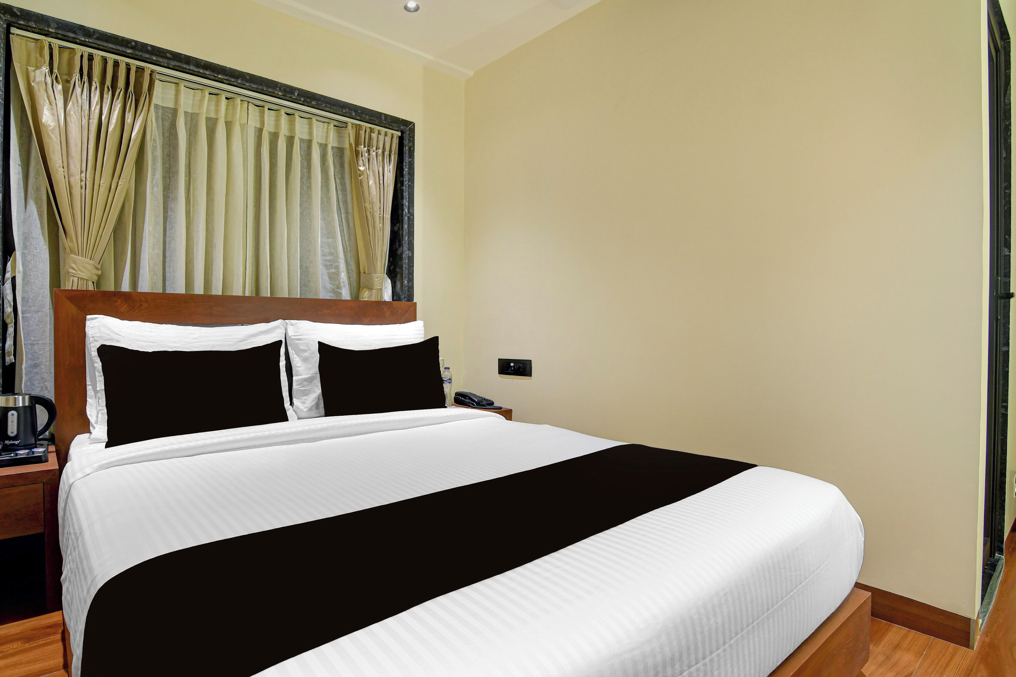 A hotel room with a large bed, a nightstand with a coffee maker, and a window with curtains.