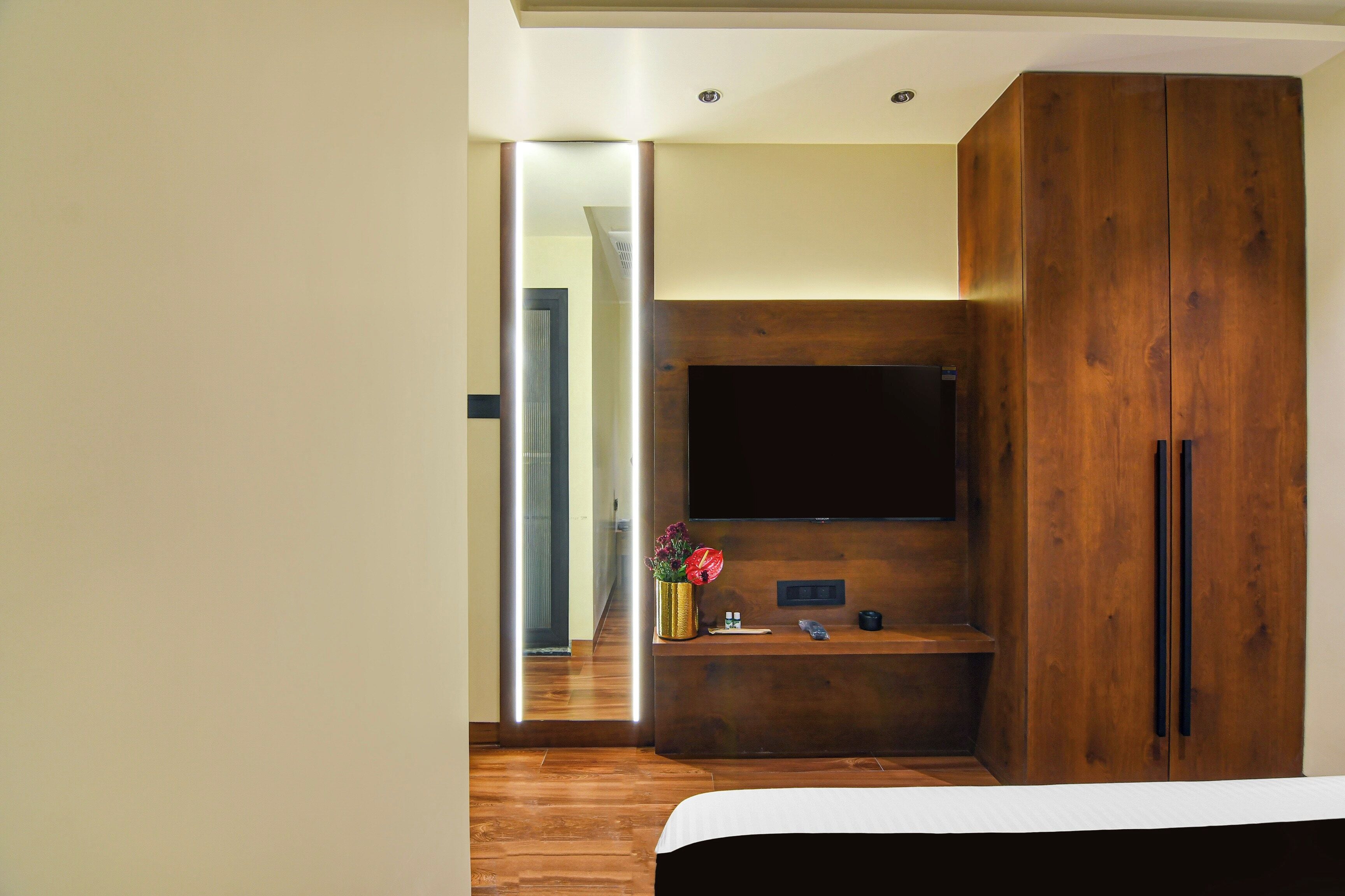 A modern bedroom with a large wooden wardrobe, a flat-screen TV mounted on the wall, and a bedside table with a vase of flowers.