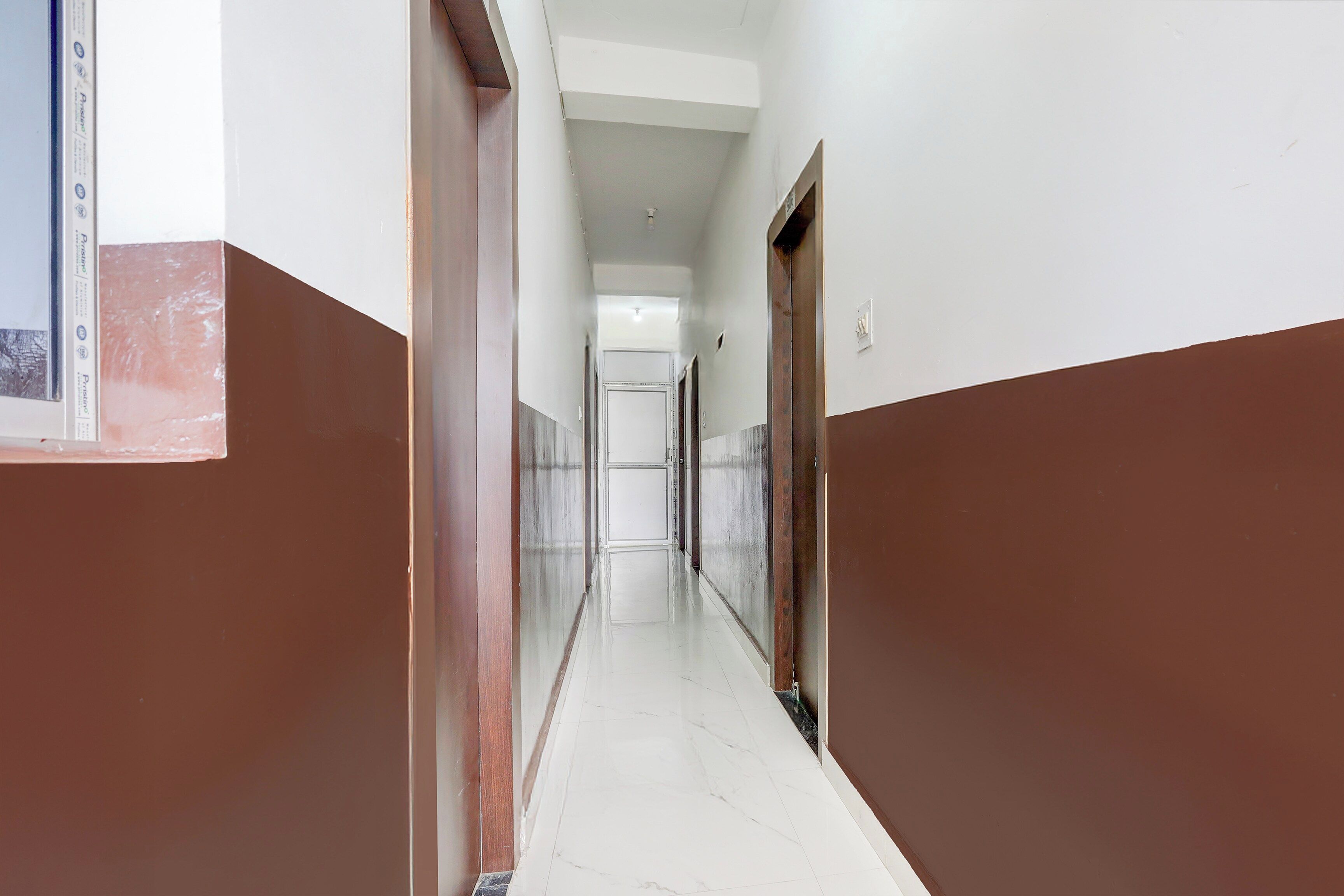 A corridor with white walls and brown trim, leading to a door at the end.