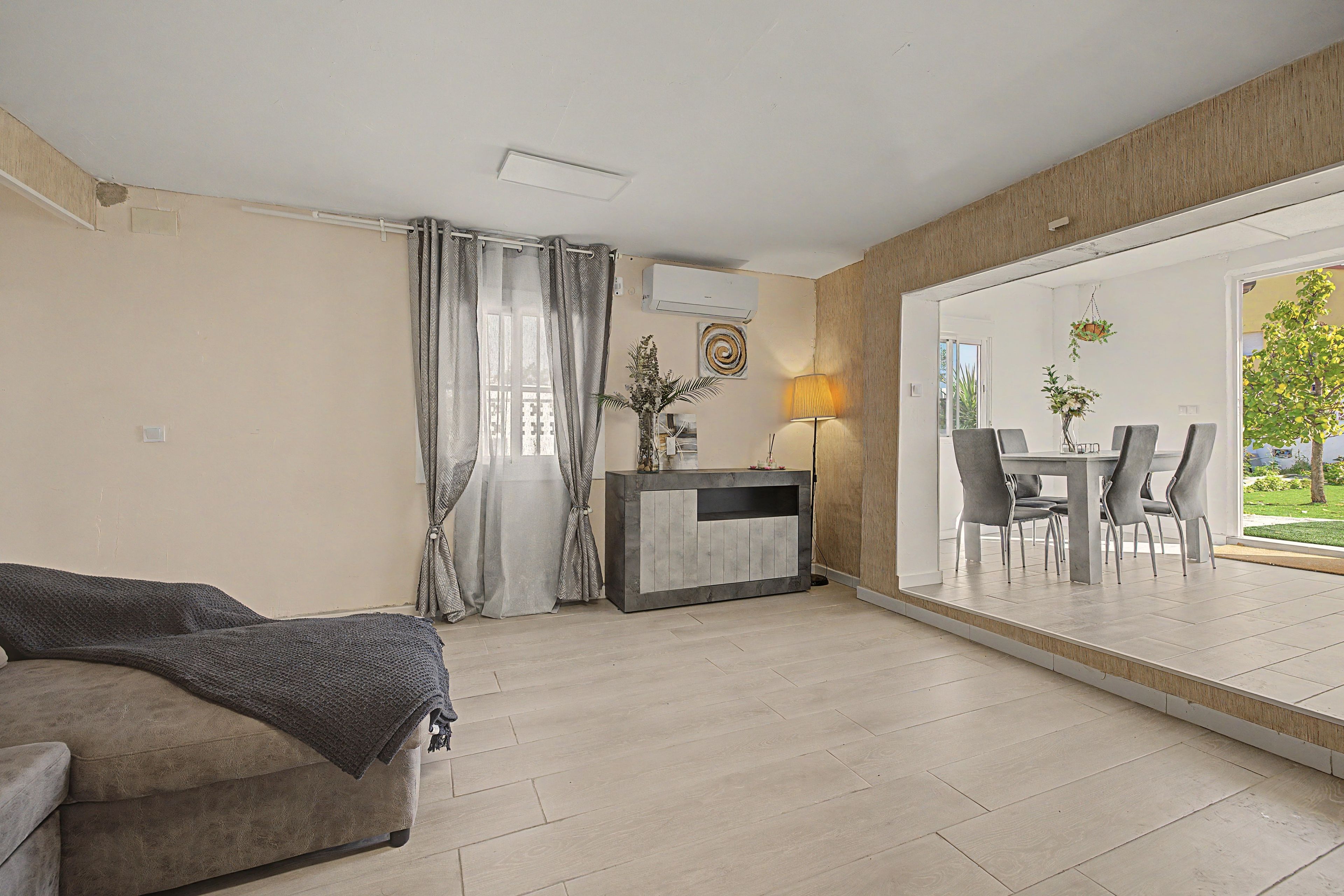 Een moderne woonkamer met een bank, een eethoek met tafel en stoelen, en een grote schuifpui naar een terras.