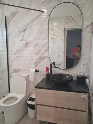 A bathroom with a toilet, sink, mirror, and marble walls.