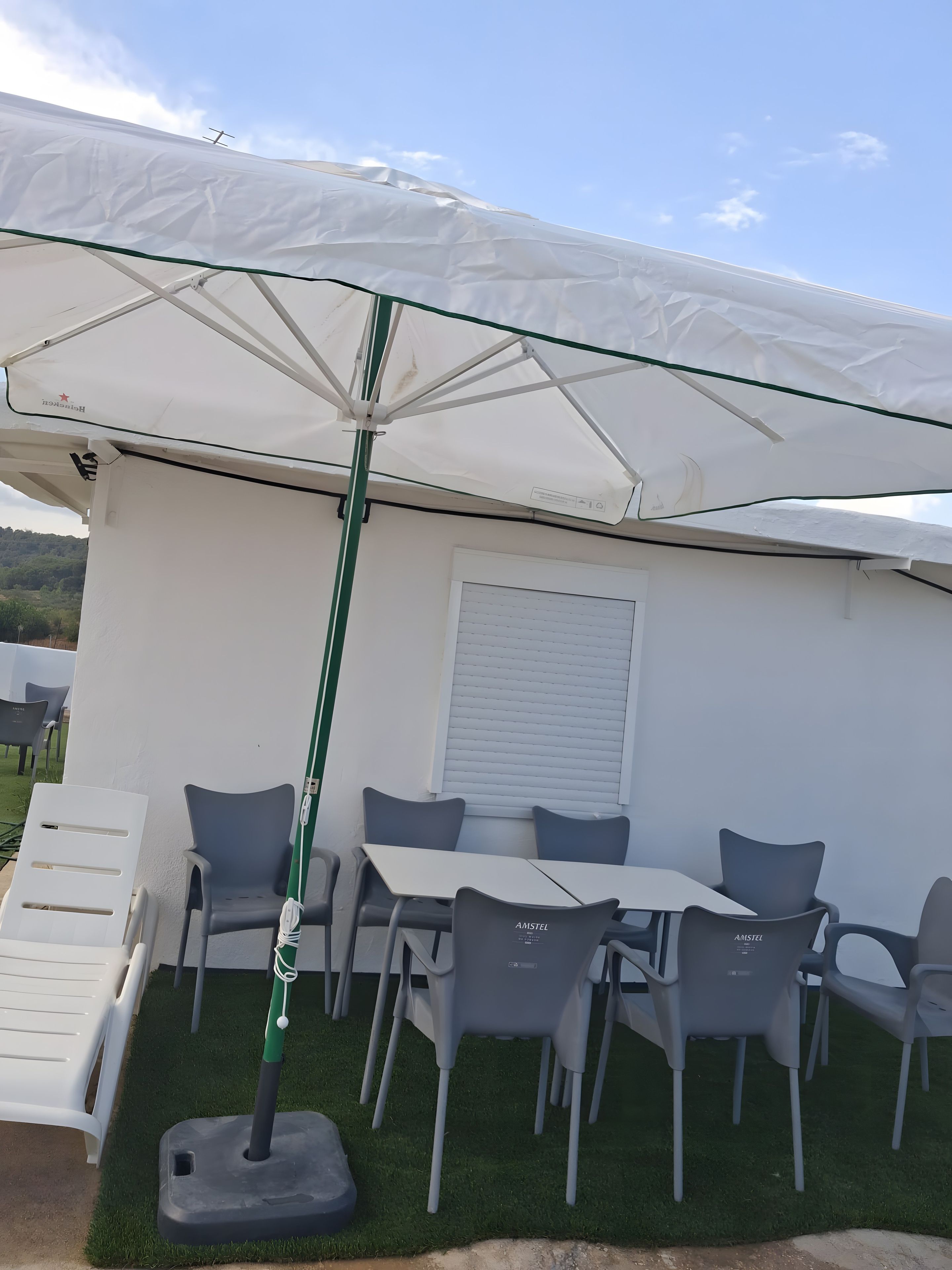 Un patio con mesa y sillas, una sombrilla y una pared blanca con una ventana.