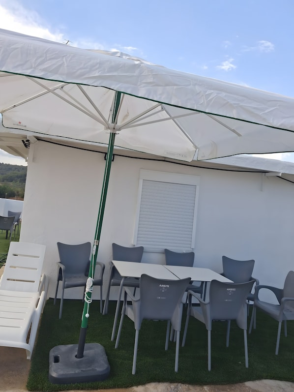 A patio area with a table and chairs, an umbrella, and a white wall with a window.
