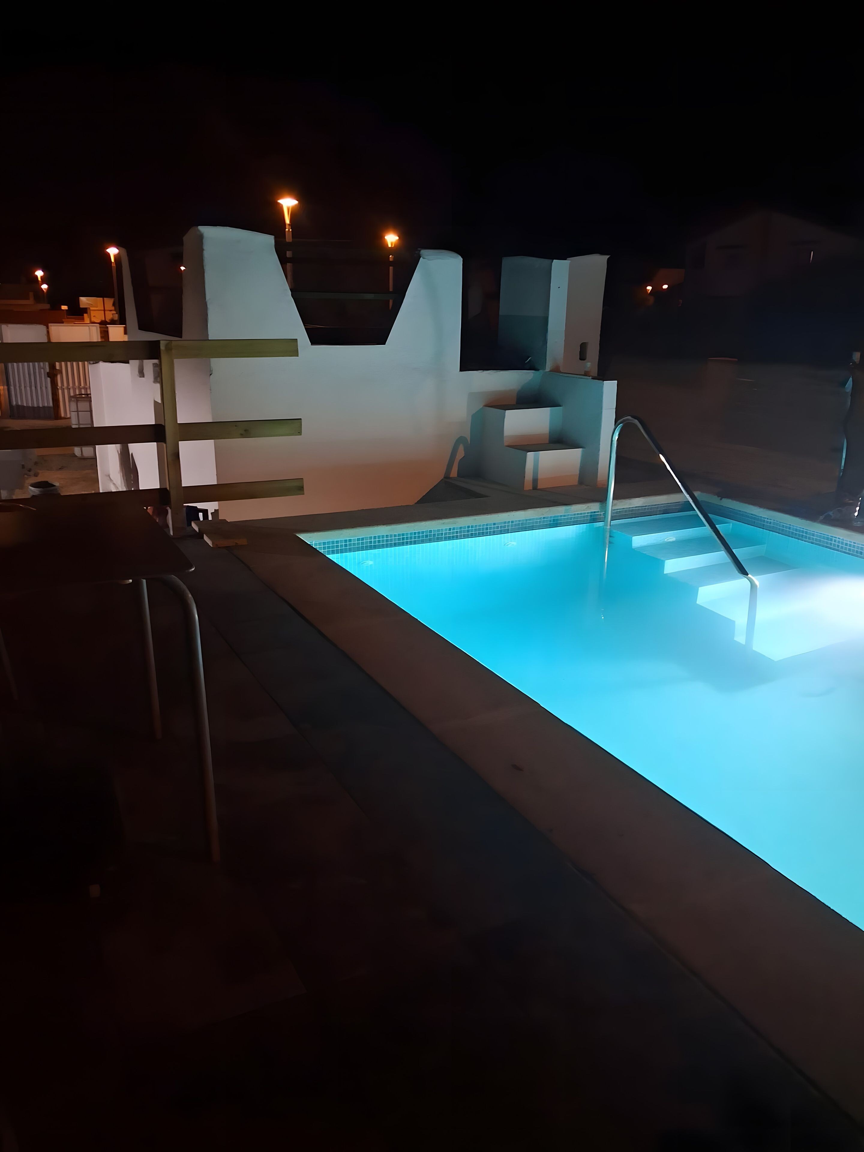A swimming pool with steps leading into it, surrounded by a modern outdoor area with a flat roof and a small seating area.