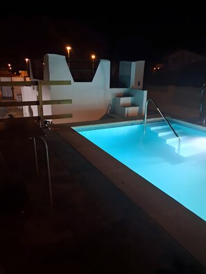 A swimming pool with steps leading into it, surrounded by a modern outdoor area with a flat roof and a small seating area.