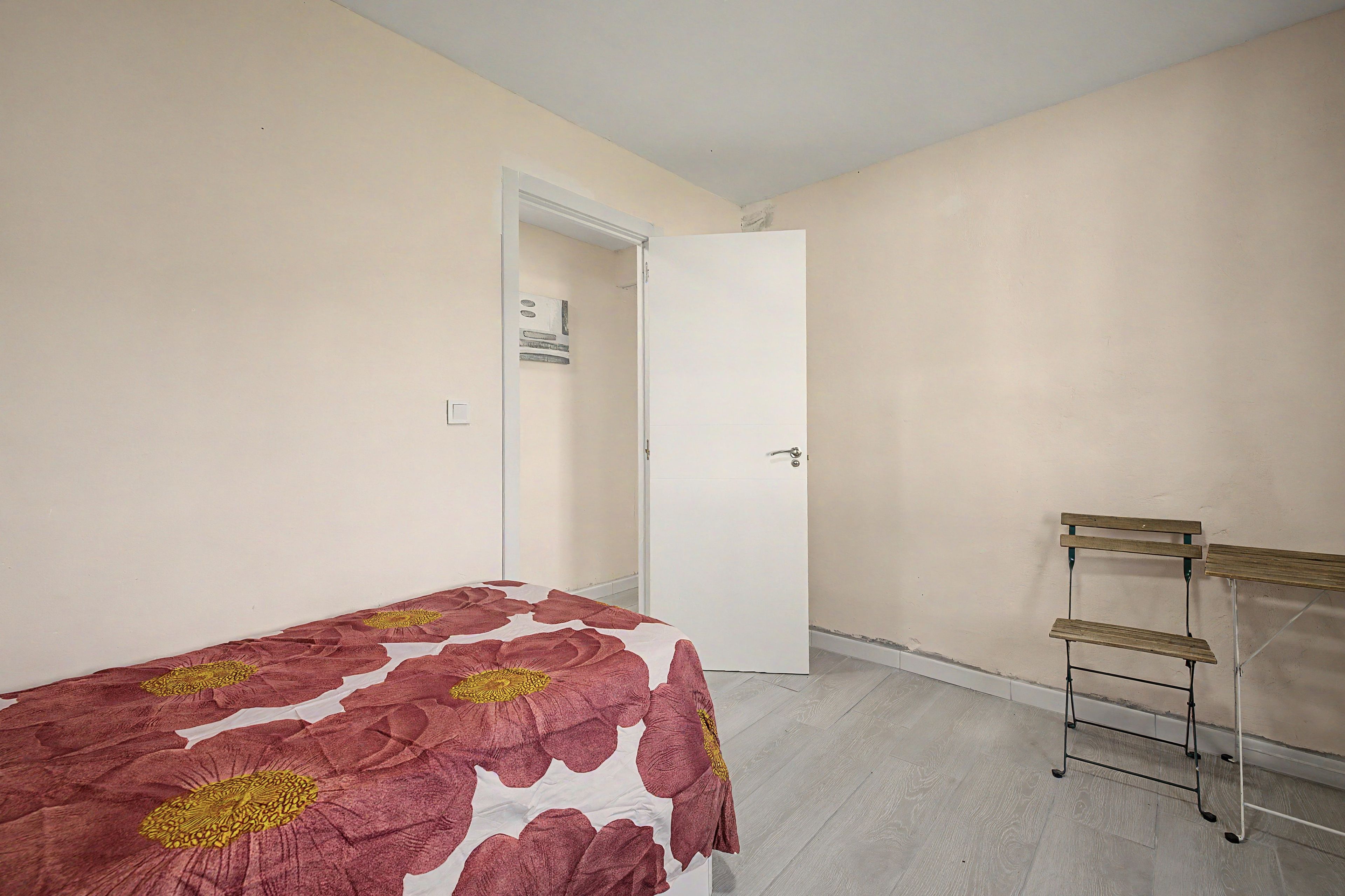 Quarto com cama, porta, prateleira na parede e piso em tons claros.