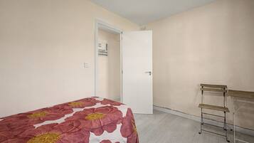 Quarto com cama, porta, prateleira na parede e piso em tons claros.