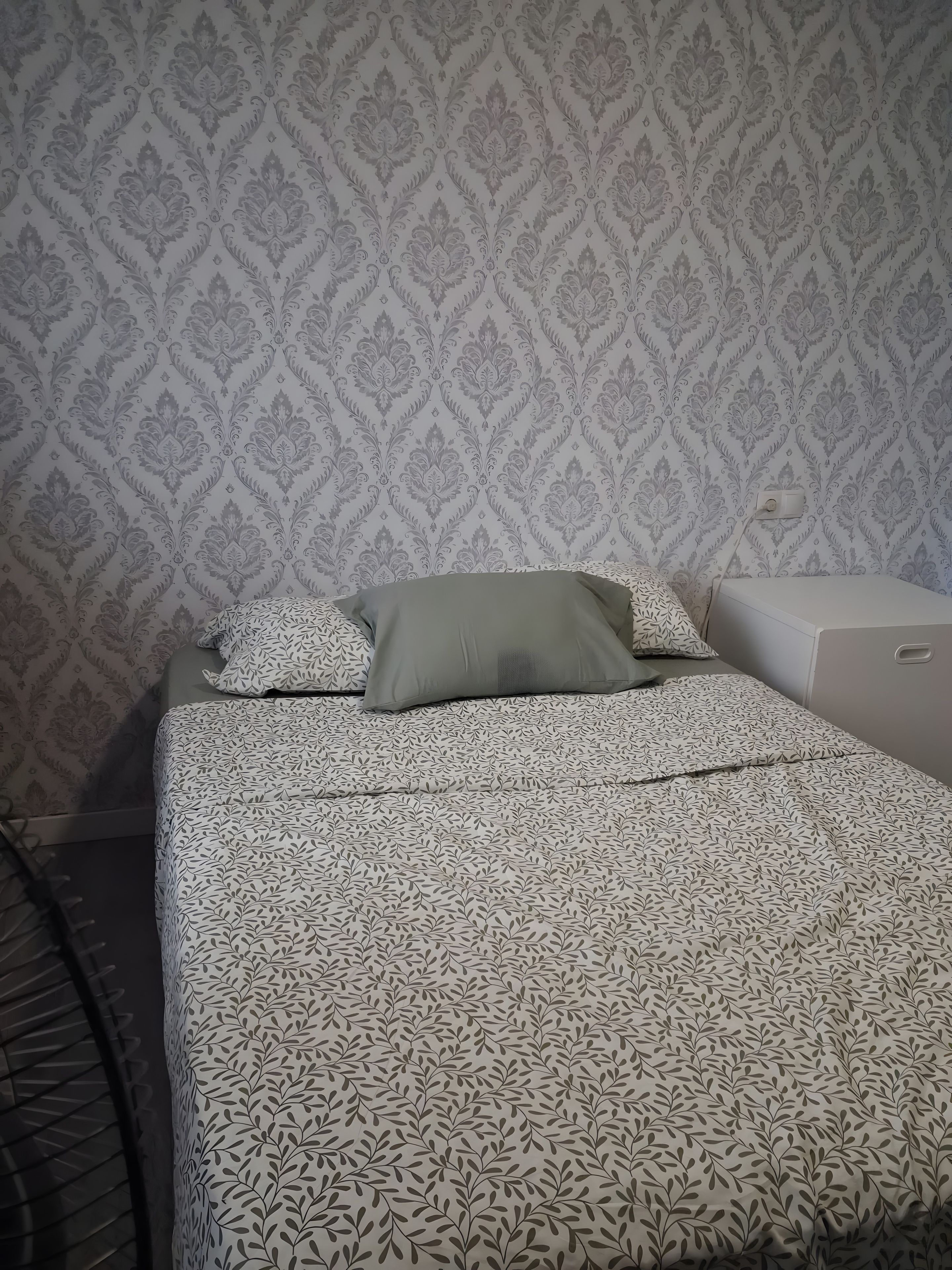 Ein Bett mit einem gemusterten Überwurf, einem Kopfkissen und einem Nachttisch.